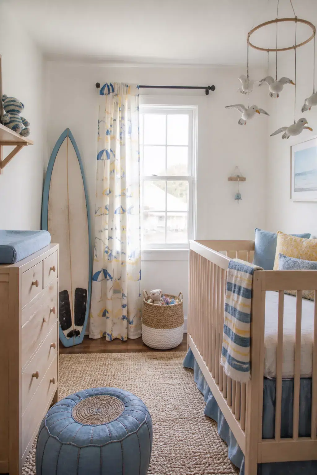 Beach themed nursery design with surfboard decor, seagull mobile, and coastal blue accents in a soft white room.