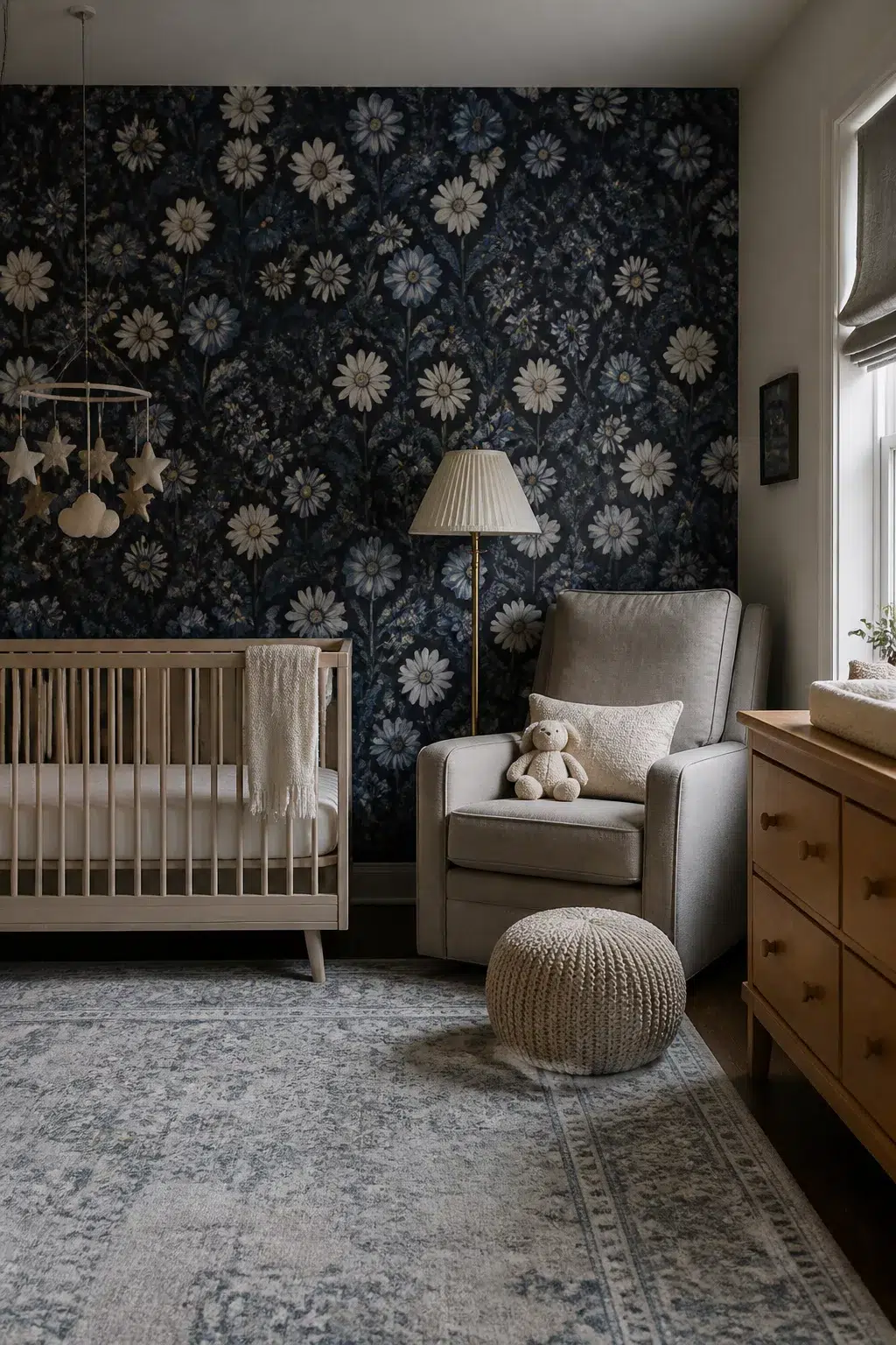 Moody dark navy blue floral nursery wallpaper with daisy print, wood crib, gray glider, and gold floor lamp.