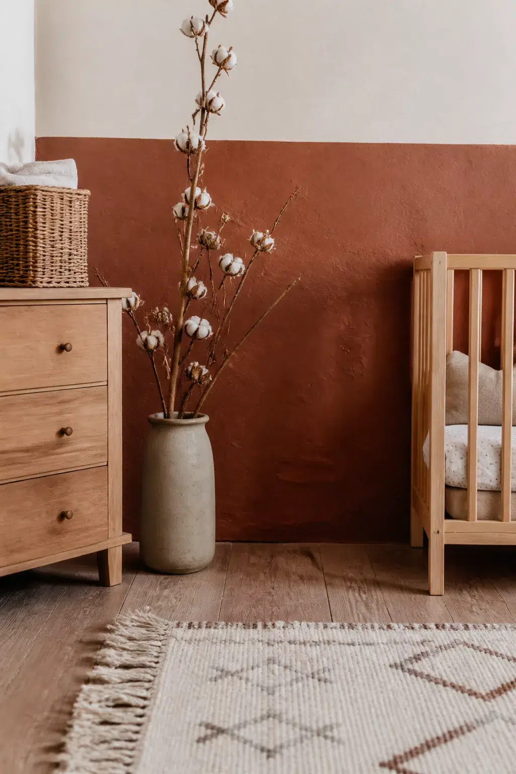 Boho accent wall nursery with terracotta half-wall plaster finish, wood crib, dresser, and cotton stem vase
