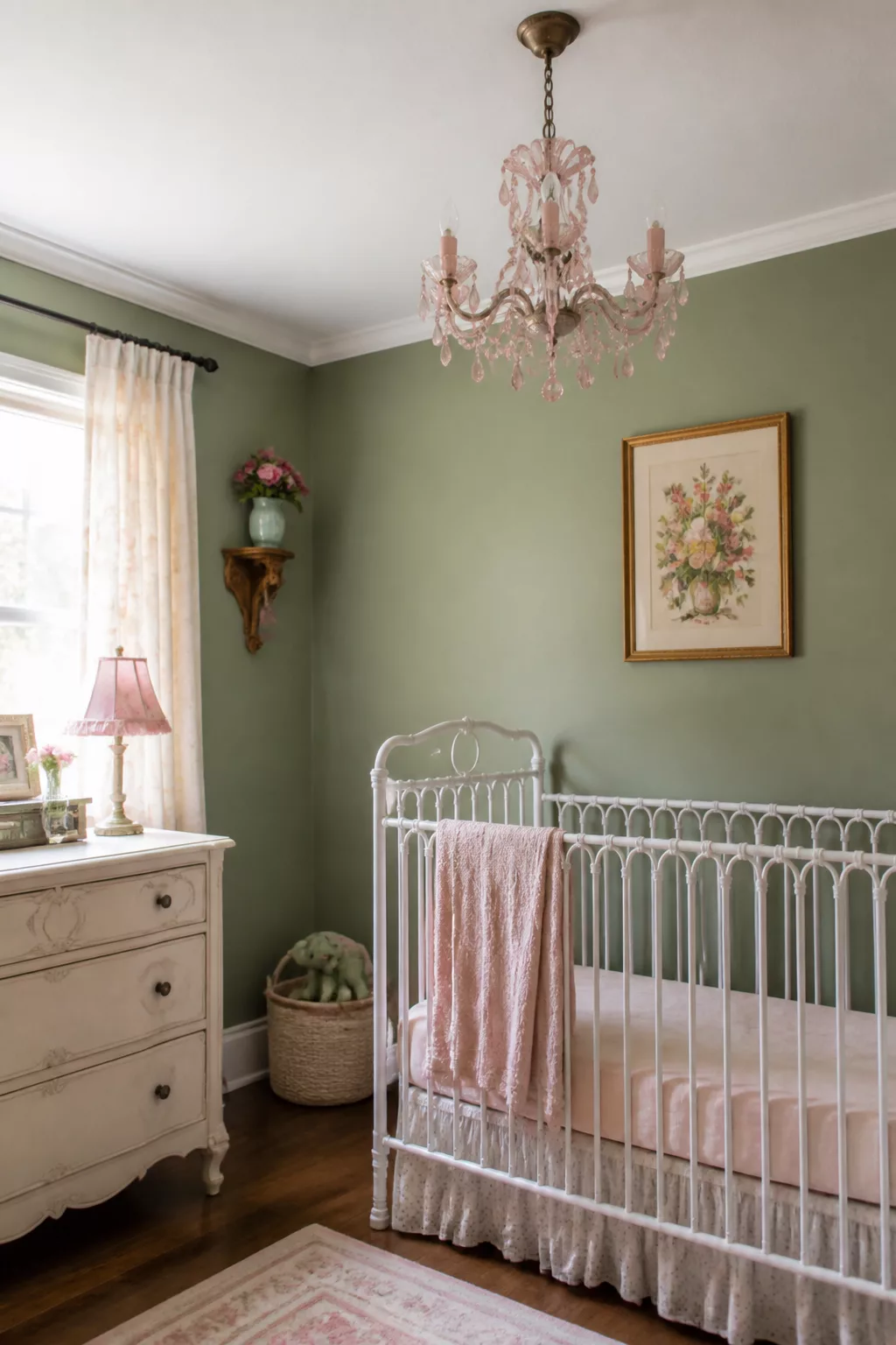 Sage green and pink nursery with a crystal chandelier, white iron crib, and vintage dresser — green and pink nursery designs.