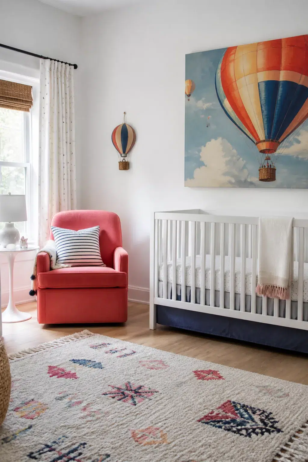 Hot air balloon nursery ideas with coral glider, oversized balloon canvas art, and navy crib skirt accents.