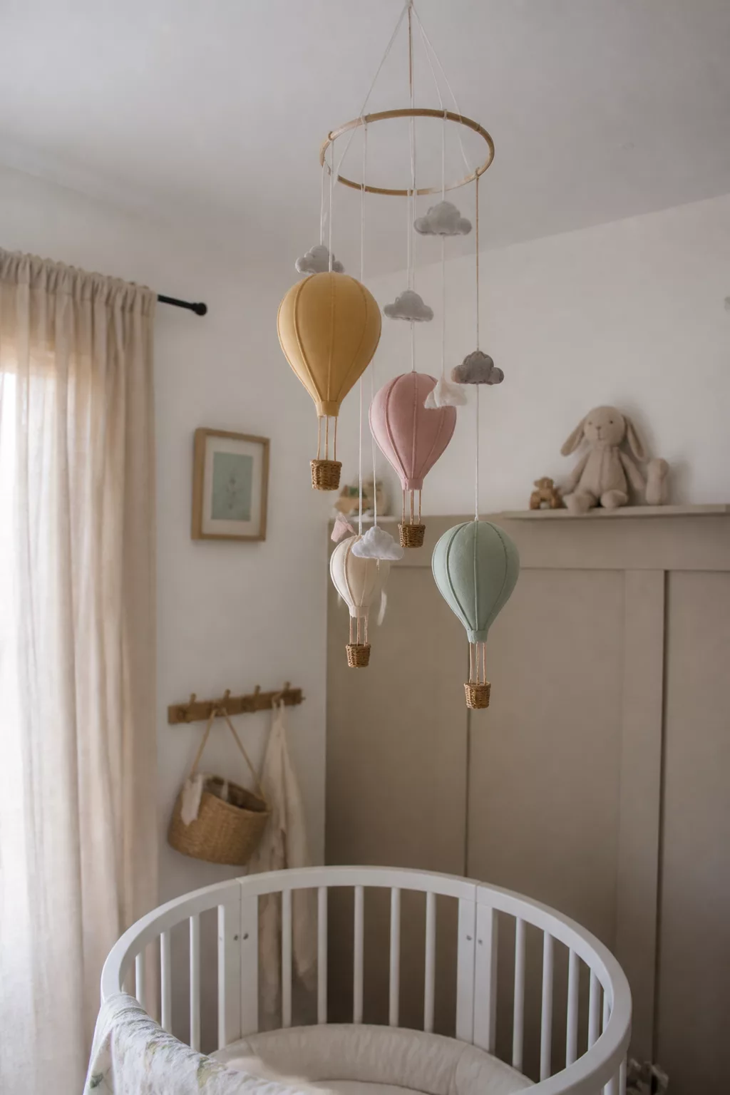 Felt hot air balloon mobile in mustard, blush, and sage over a round white crib — hot air balloon nursery ideas