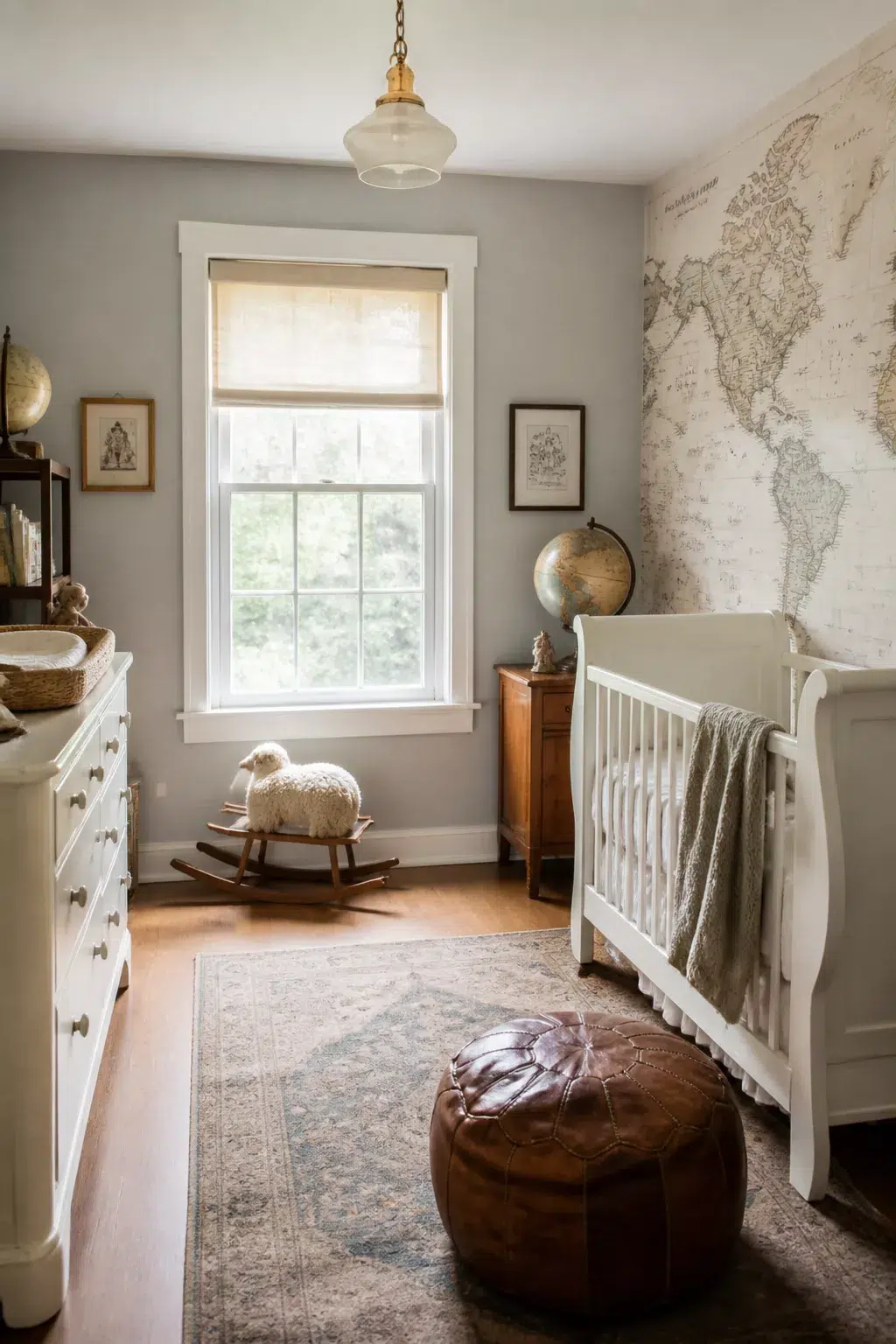 Soft gray vintage style nursery with world map wallpaper, white sleigh crib, leather pouf, and antique globe.